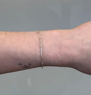 Silver chain with gold beads on a person's wrist on grey background