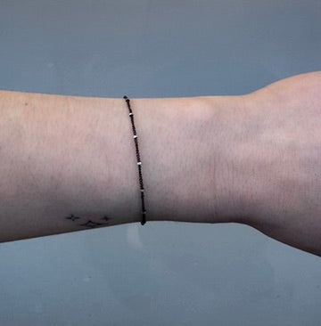 Black chain with silver beads on a person's wrist on grey background