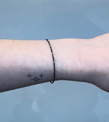 Black chain with silver beads on a person's wrist on grey background