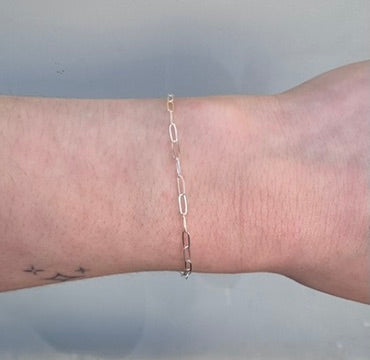 Silver paperclip chain on a person's wrist on a white background