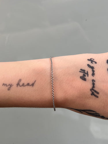 Bracelet on a wrist with tattoos against a gray background
