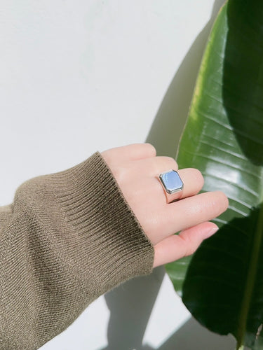 Hand wearing a ring with a blue stone against a white background