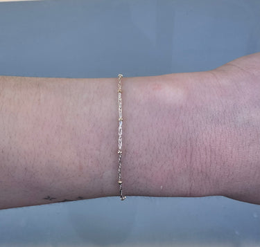 Silver chain with gold beads on a person's wrist on grey background