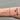 Bracelet on a wrist with tattoos against a gray background