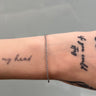 Bracelet on a wrist with tattoos against a gray background