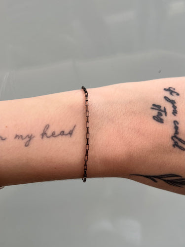 black box link silver chain on a wrist against a neutral background