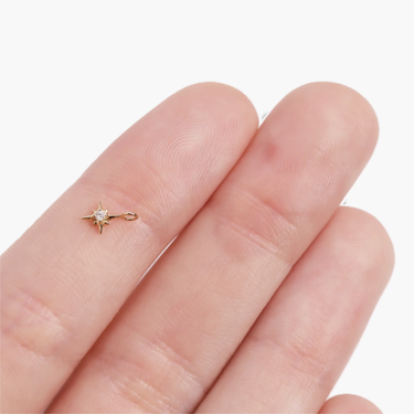 A 14k yellow gold north star charm with a natural diamond, finger for scale (smaller than pinky nail).