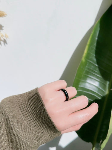 Hand wearing a black ring on a light background with green leaves