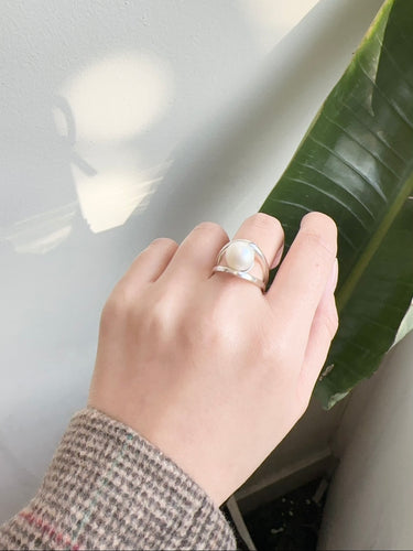 Hand wearing a silver ring with a green leaf in the background