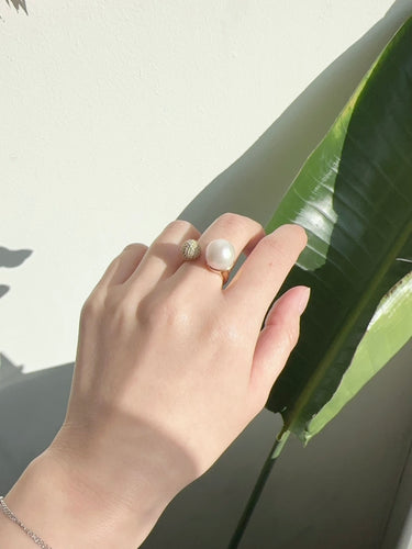 Hand wearing a pearl ring with a leaf background