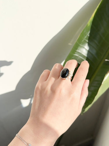 Hand wearing a black ring with a green leaf background