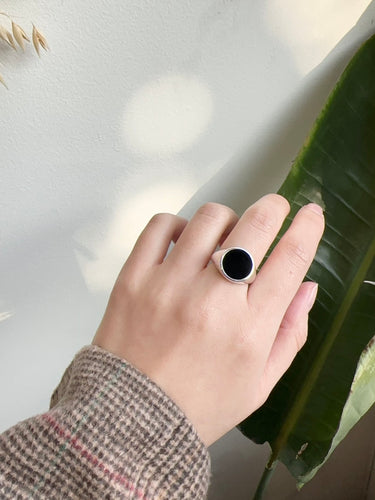 Hand wearing a silver ring with a black stone against a light background